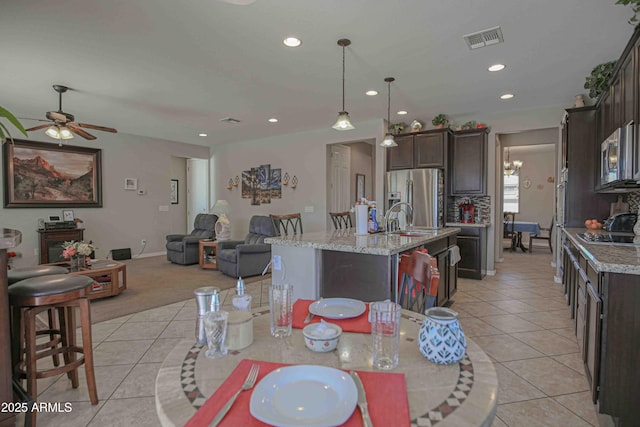 kitchen with light tile patterned flooring, visible vents, open floor plan, dark brown cabinets, and appliances with stainless steel finishes