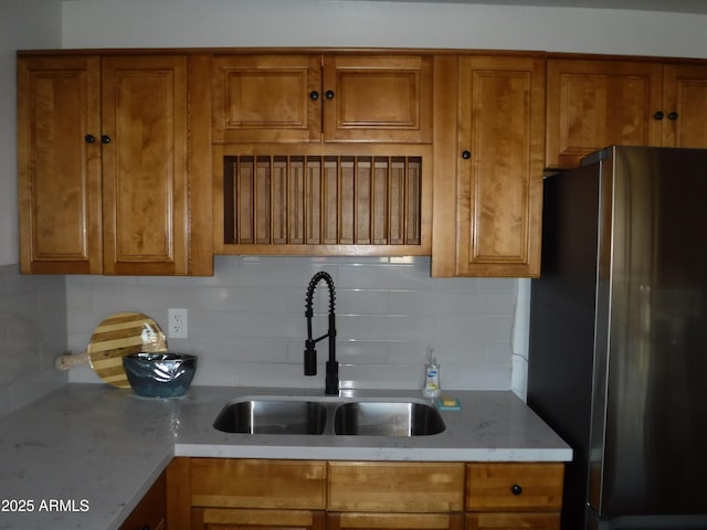 kitchen with light stone counters, sink, tasteful backsplash, and stainless steel refrigerator