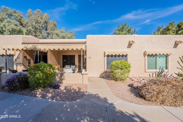 pueblo revival-style home with stucco siding, a garage, and a patio area