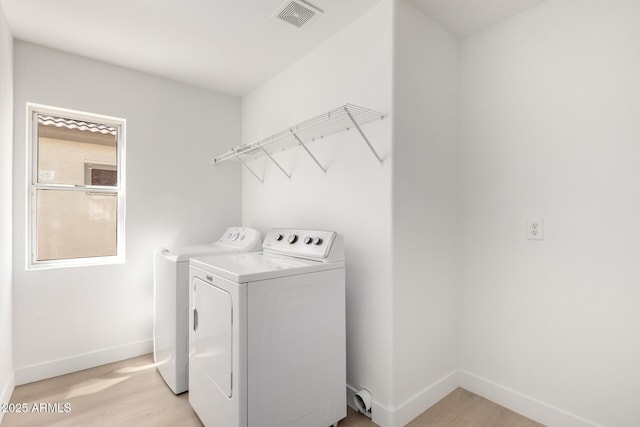 clothes washing area featuring baseboards, visible vents, light wood-style floors, washer and dryer, and laundry area