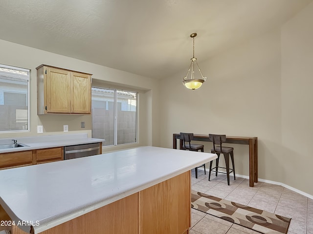 kitchen featuring light brown cabinetry, stainless steel dishwasher, pendant lighting, a kitchen island, and light tile patterned flooring