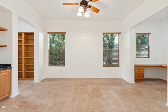 unfurnished living room featuring light tile patterned floors, built in desk, plenty of natural light, and ceiling fan