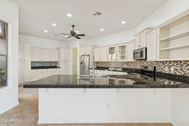 kitchen with kitchen peninsula, a kitchen bar, stainless steel appliances, sink, and dark stone countertops