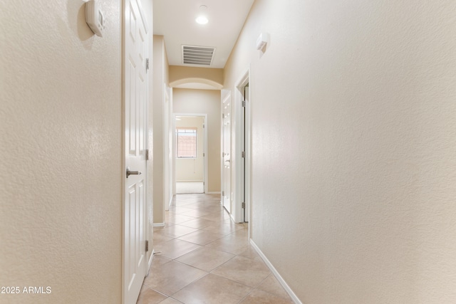 hallway featuring light tile patterned floors, arched walkways, visible vents, and baseboards