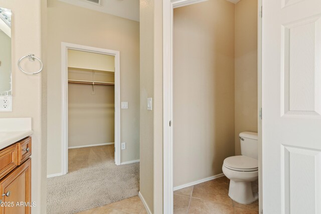 bathroom featuring a walk in closet, baseboards, toilet, tile patterned floors, and vanity