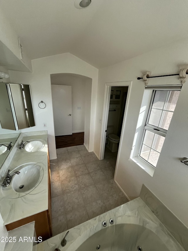 bathroom with a tub, vanity, vaulted ceiling, and toilet