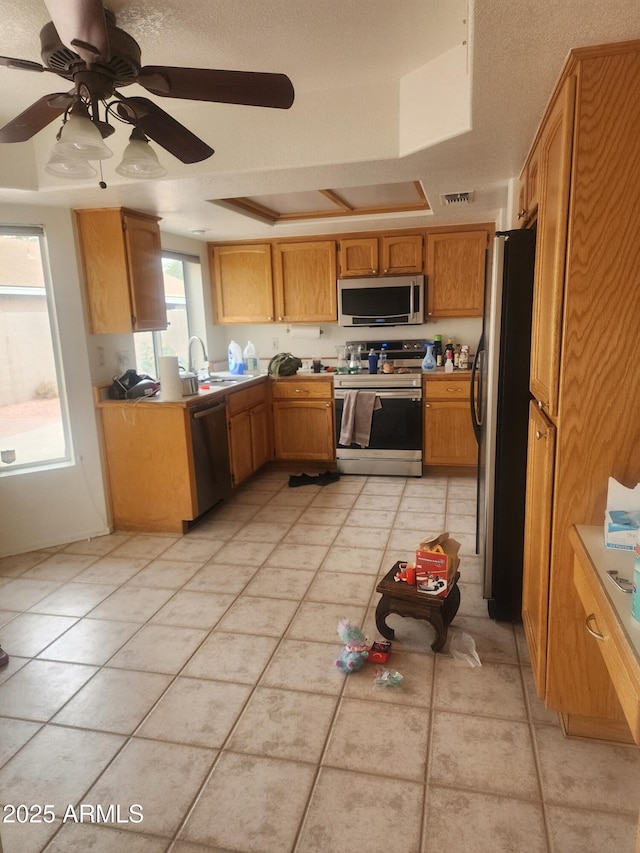 kitchen with a raised ceiling, sink, ceiling fan, light tile patterned floors, and appliances with stainless steel finishes