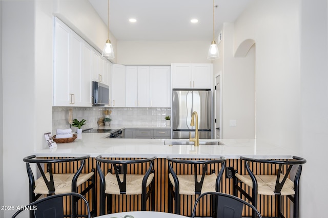 kitchen featuring stainless steel appliances, a kitchen breakfast bar, kitchen peninsula, and white cabinets