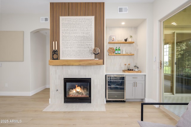 bar featuring wine cooler, a fireplace, and light hardwood / wood-style flooring