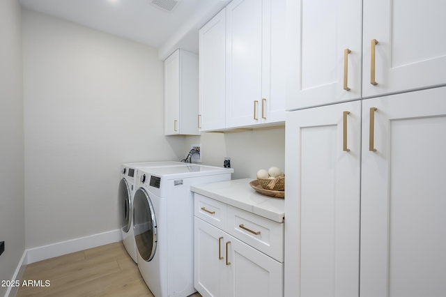 clothes washing area with independent washer and dryer, cabinets, and light wood-type flooring