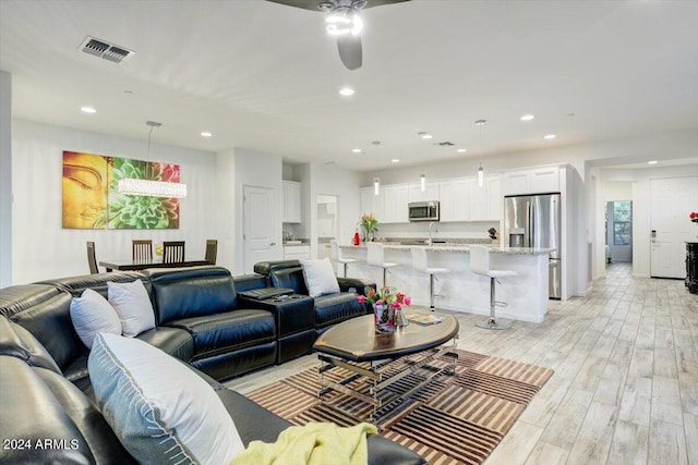 living room featuring ceiling fan, sink, and light hardwood / wood-style flooring