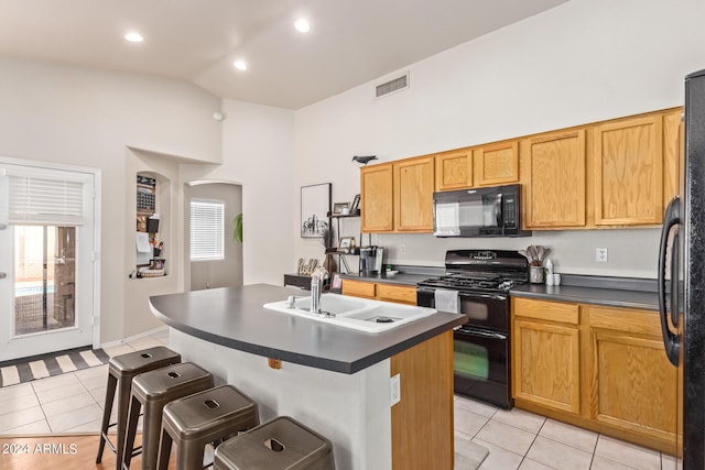 kitchen featuring light tile patterned floors, black appliances, a breakfast bar, and a center island with sink