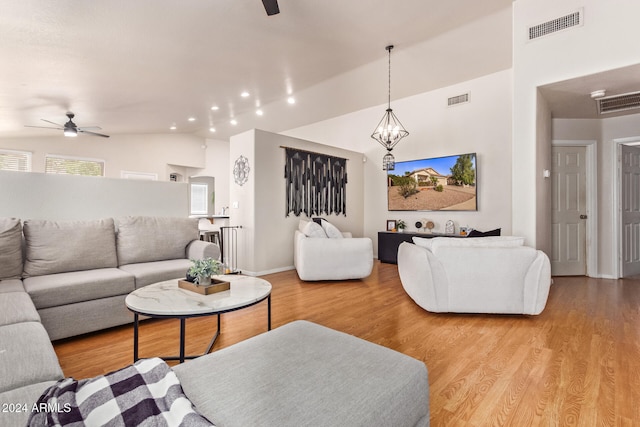 living room featuring lofted ceiling, ceiling fan with notable chandelier, and light hardwood / wood-style floors