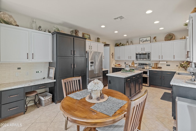 kitchen featuring stainless steel appliances, light tile patterned floors, a center island, and white cabinetry