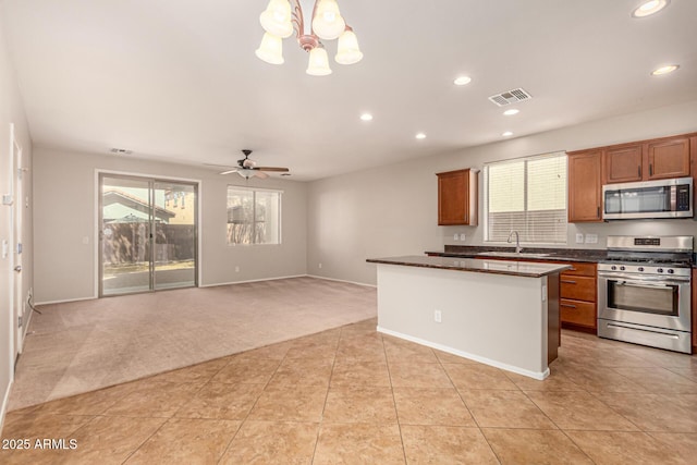 kitchen with visible vents, dark countertops, stainless steel appliances, a kitchen island, and light colored carpet