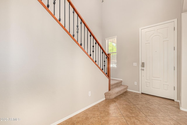 foyer entrance with stairway, light tile patterned floors, a high ceiling, and baseboards