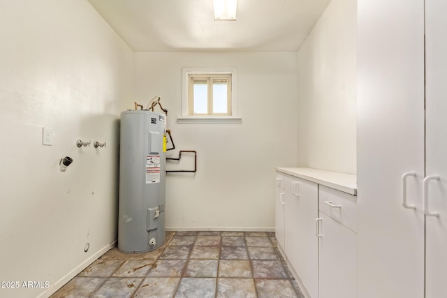 laundry room with water heater, cabinet space, stone finish flooring, and baseboards