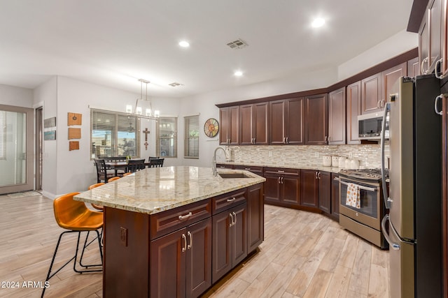 kitchen with appliances with stainless steel finishes, sink, a kitchen bar, light wood-type flooring, and a center island with sink