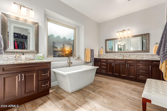 bathroom featuring vanity, tasteful backsplash, wood-type flooring, and a bath