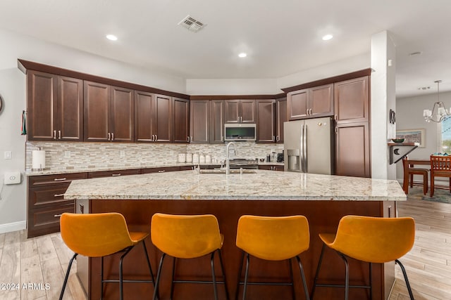 kitchen with light hardwood / wood-style flooring, a kitchen island with sink, stainless steel appliances, and backsplash