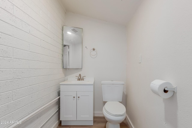 bathroom with hardwood / wood-style flooring, vanity, brick wall, and toilet