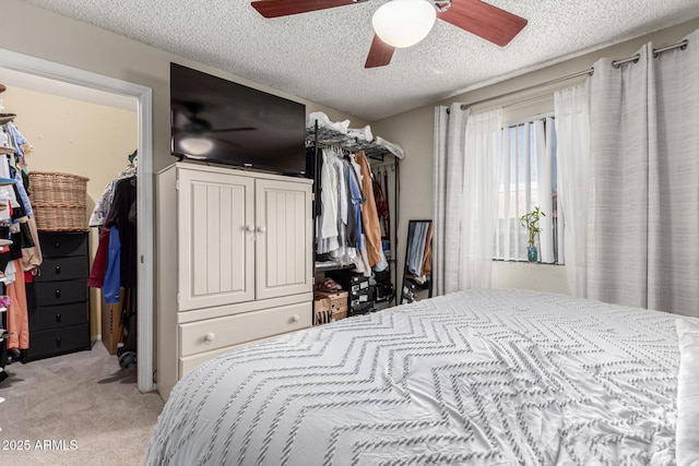 bedroom featuring a walk in closet, ceiling fan, light carpet, and a textured ceiling