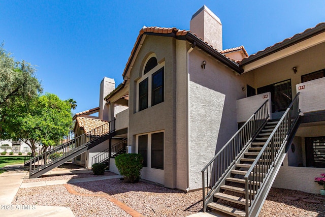 view of side of home with stairs, stucco siding, a tile roof, and a chimney