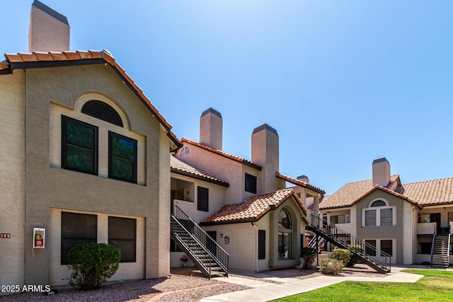 view of front of home with a tiled roof, a chimney, stairs, and stucco siding