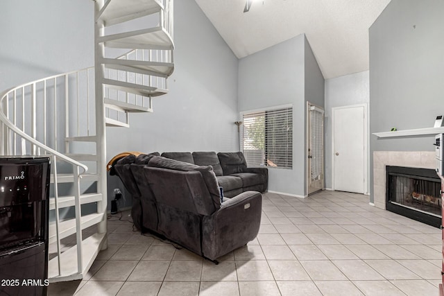 living area with stairs, light tile patterned flooring, high vaulted ceiling, and a tile fireplace