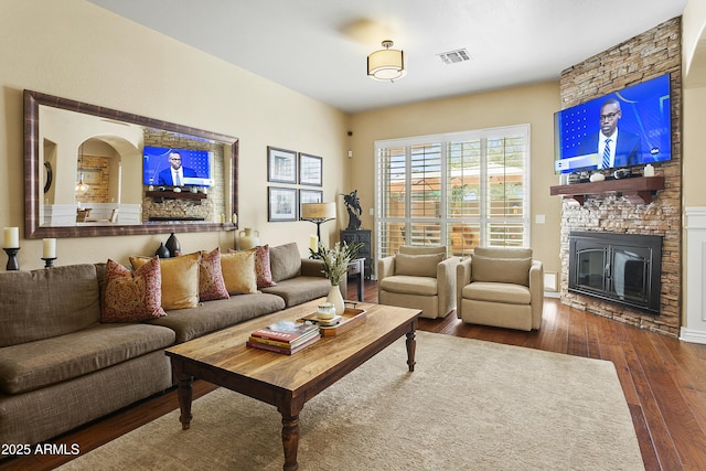 living area featuring dark wood-style flooring, visible vents, and a fireplace