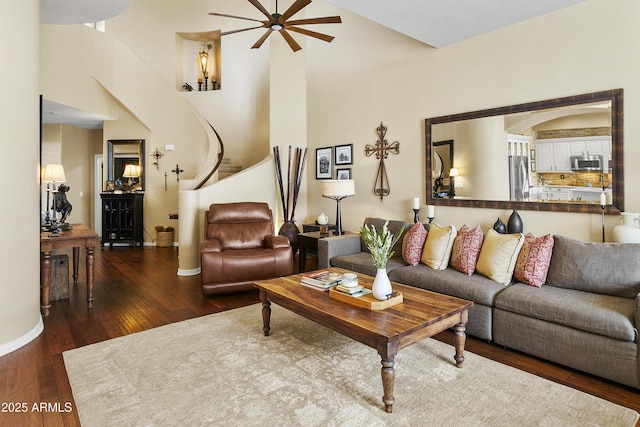 living room with a towering ceiling, baseboards, a ceiling fan, and wood finished floors