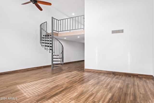 unfurnished living room with ceiling fan, hardwood / wood-style floors, and a high ceiling