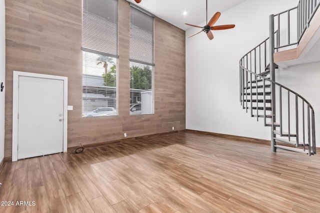 unfurnished living room featuring ceiling fan, light hardwood / wood-style flooring, a towering ceiling, and wooden walls