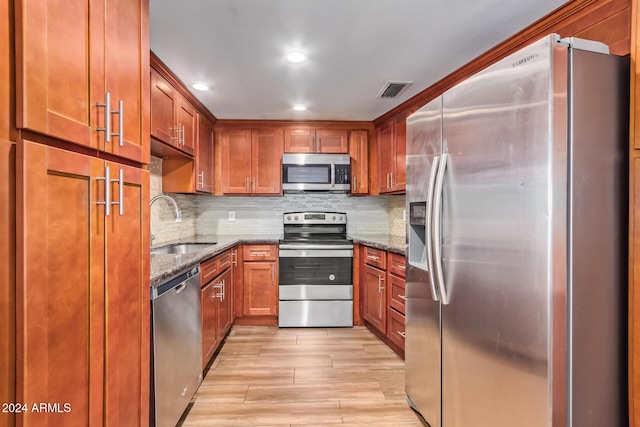 kitchen with sink, light hardwood / wood-style floors, dark stone countertops, and stainless steel appliances