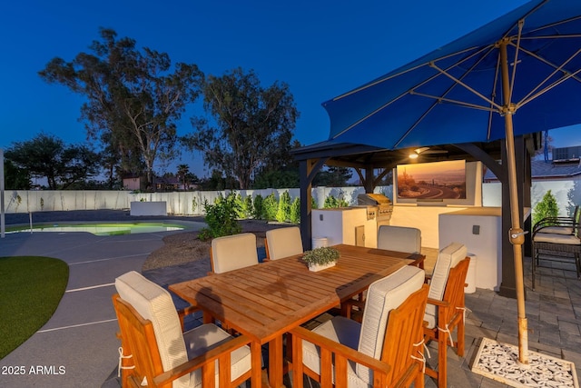 patio at twilight with an outdoor kitchen, a fenced backyard, outdoor dining space, and a grill