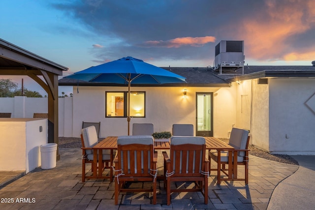 back of house at dusk with a patio, outdoor dining area, and stucco siding