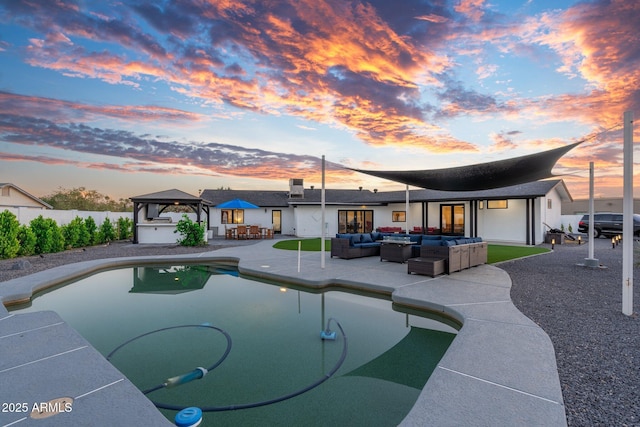 pool at dusk featuring outdoor lounge area, fence, a fenced in pool, a patio area, and a gazebo