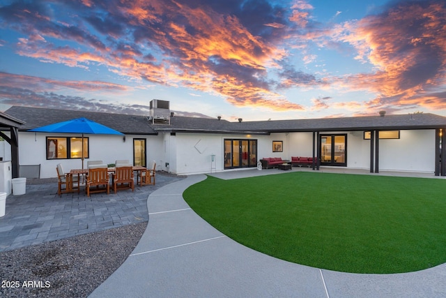 back of property at dusk with a patio area, stucco siding, a yard, and an outdoor hangout area