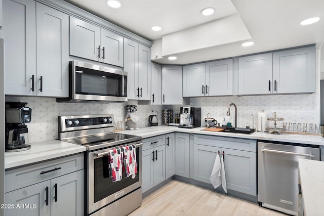 kitchen with a sink, appliances with stainless steel finishes, gray cabinets, and tasteful backsplash
