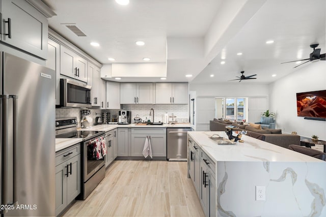 kitchen with gray cabinets, visible vents, a sink, open floor plan, and stainless steel appliances