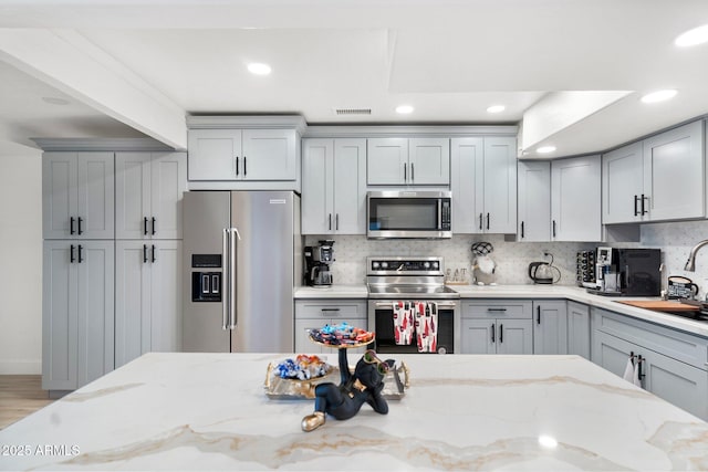 kitchen with decorative backsplash, recessed lighting, a sink, gray cabinetry, and stainless steel appliances