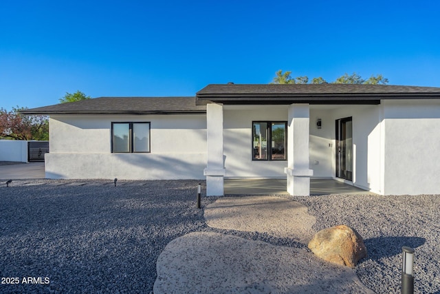 view of front facade with a patio area, stucco siding, and roof with shingles