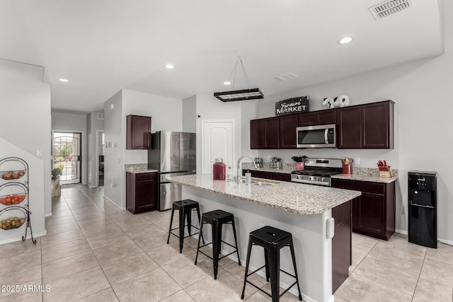 kitchen featuring visible vents, a sink, dark brown cabinetry, appliances with stainless steel finishes, and a kitchen bar