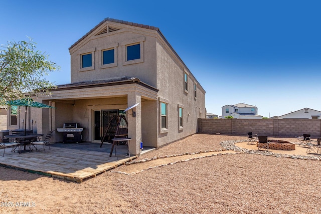 rear view of house featuring stucco siding, a patio area, a fenced backyard, and an outdoor fire pit