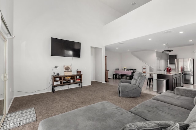 living room featuring visible vents, light carpet, recessed lighting, baseboards, and a towering ceiling