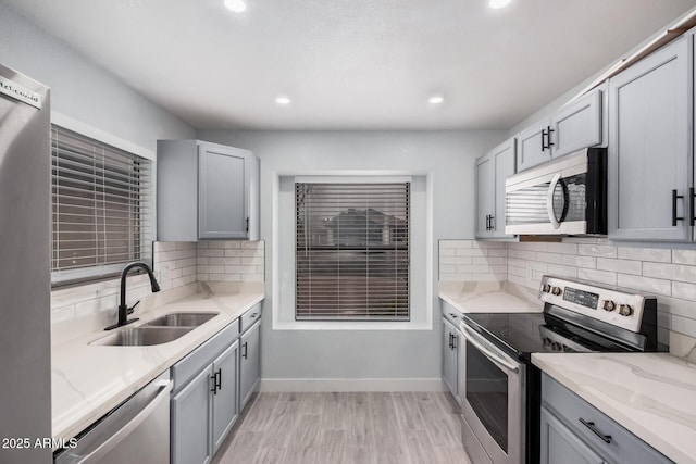 kitchen featuring appliances with stainless steel finishes, gray cabinets, sink, and light stone countertops