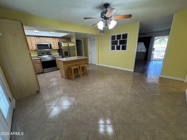 11221 N 91st Dr, Peoria, AZ 85345 - kitchen with appliances with stainless steel finishes, light tile patterned floors, a center island, a ceiling fan, and baseboards