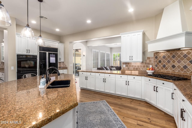 kitchen featuring sink, decorative light fixtures, black appliances, custom range hood, and light wood-type flooring