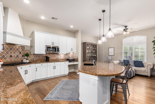 kitchen featuring pendant lighting, premium range hood, white cabinetry, appliances with stainless steel finishes, and light wood-type flooring