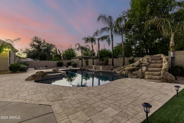 pool at dusk featuring an in ground hot tub and a patio